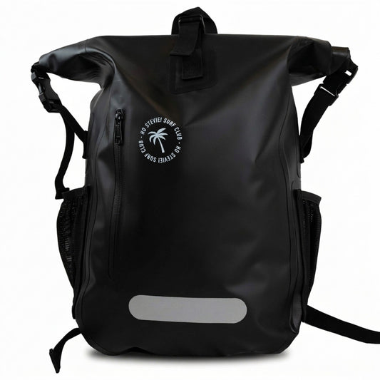 A black waterproof roll-top backpack with a white circular logo on the front pocket that reads 'SANTA FEDELA SURF CLUB' with a palm tree graphic. The bag features a silver reflective strip near the bottom, side mesh pockets, and a top carry handle, shown against a plain white background.